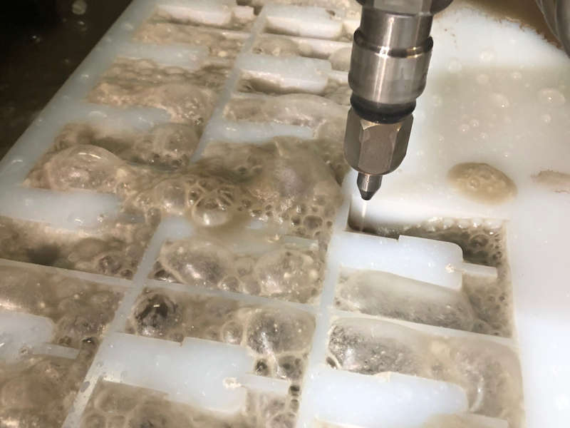 waterjet cutting machine cutting plastic pieces with brown bubbles between holes